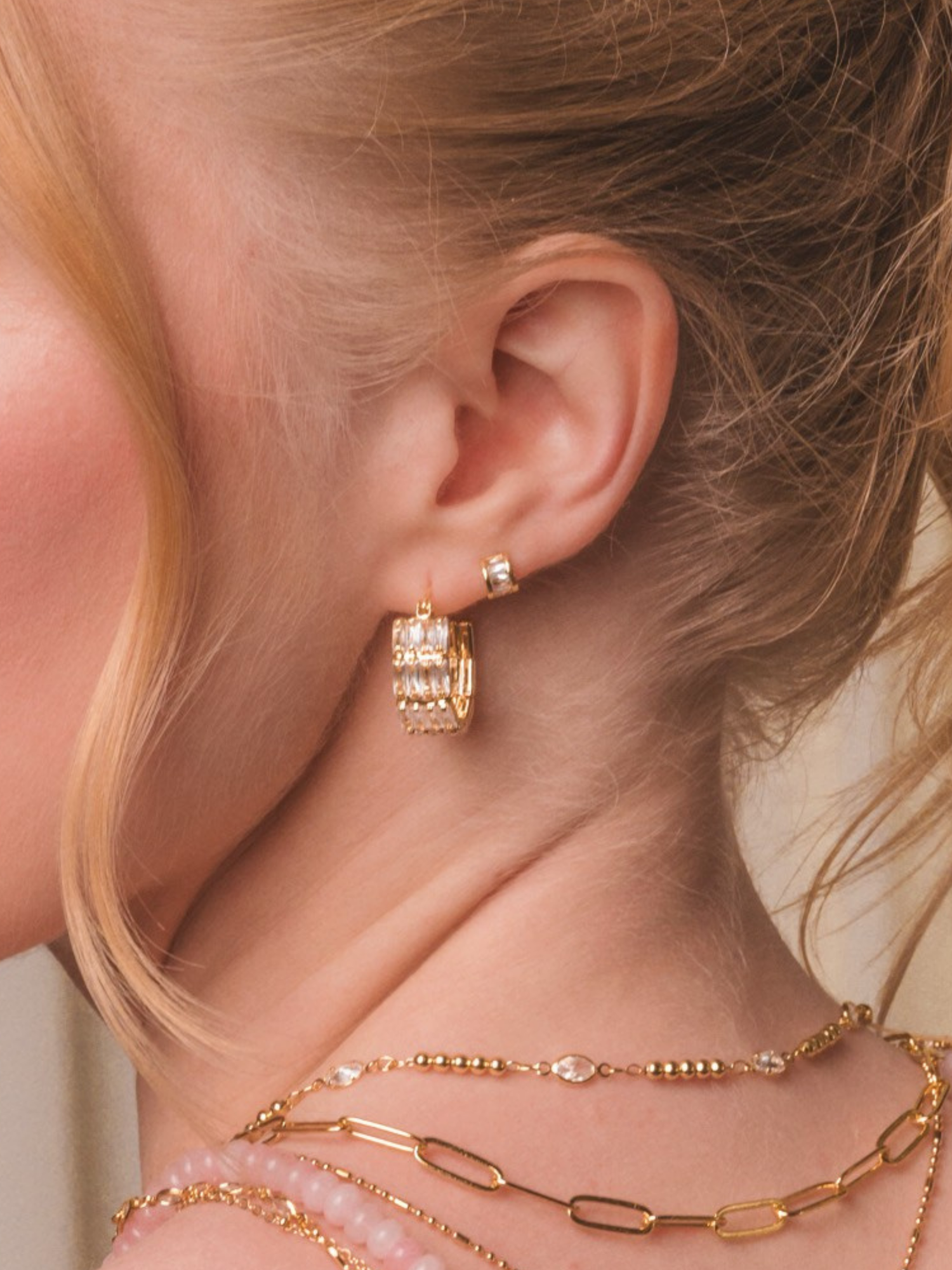 woman's ear wearing two small diamond hoop earrings and blue flowers laying on her shoulder
